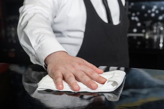 The hand of a professional bartender wipes the bar counter with a napkin or cloth, cleans and prepares the workplace