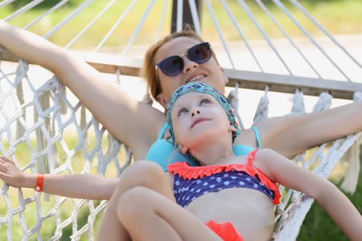 Portrait of mother and daughter lay on hammock in shade, enjoy life, time with family, mother daughter time. Chilling, traveling, relax, parenthood concept