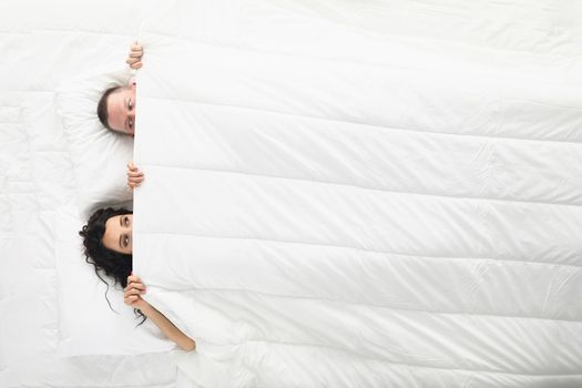 Woman and man peeking on each other under white blanket, awake couple in bed
