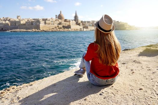 Girl sits down on the edge of the sea enjoying amazing landscape of Valletta, Malta. Travel concept with independent people doing outdoor leisure activity and wanderlust life.