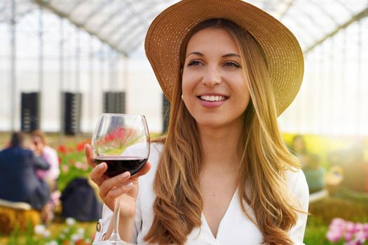 Image of cute young woman enjoying sitting in greenhouse holding glass drinking wine