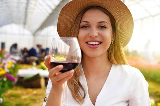 Photo of happy cheerful woman holds wine glass makes toast looking at camera isolated on greenhouse background