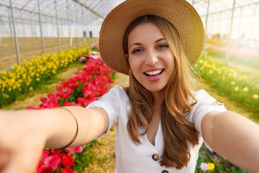 Cheerful happy young hispanic woman in greenhouse take selfie by camera on springtime