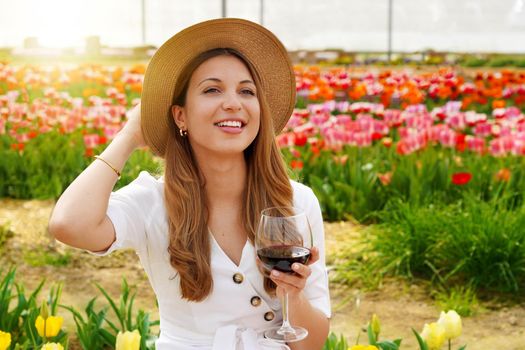 Portrait of pretty woman drinking glass of red wine over flowered background looking to the side with happy face smiling