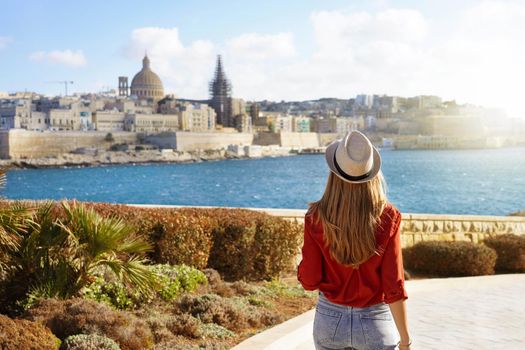 Attractive woman with hat goes down along Malta waterfront looking at beautiful cityscape of Valletta, Malta