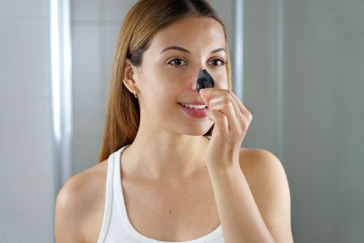 Beauty woman removing black charcoal nose strip looking satisfied
