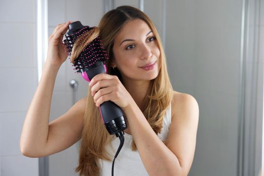 Girl using round brush hair dryer to style hair at the mirror in an easy way at home