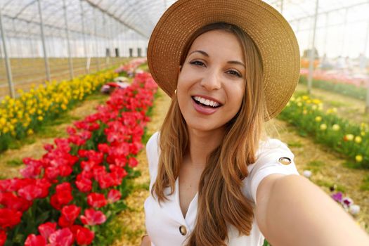 Brazilian girl laughing taking self portrait between tulips. Content creator showing greenhouse on springtime in her stories on mobile app.