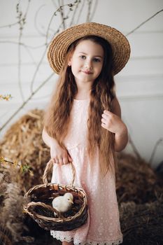 Girl in dress and hay hat keeping basket with little chick