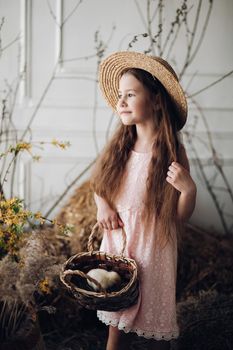 Girl in dress and hay hat keeping basket with little chick
