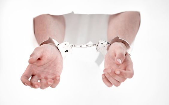 Handcuffs on the hands of a man breaking a paper wall
