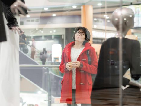 Woman stares on dummies in clothing store. Casual outfit hanging on mannequins. View through transparent shop window. Shopping at mall. Basic clothes for everyday wear. Modern urban fashion.
