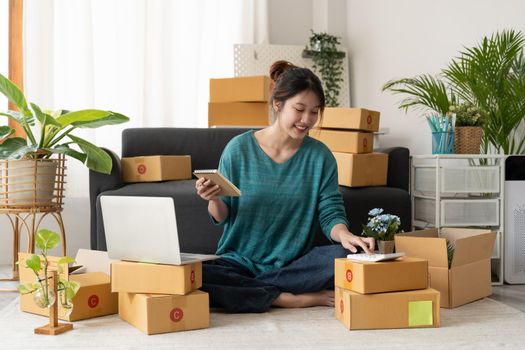 Asian woman entrepreneur using calculator with pencil in her hand, calculating financial expense at home office,online market packing box delivery,Startup successful small business owner, SME, concept