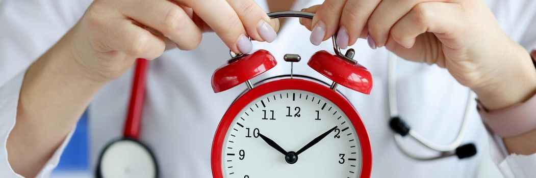 Doctor holding red alarm clock in clinic closeup