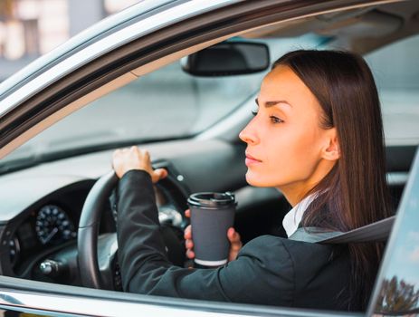 young businesswoman holding disposable coffee cup driving car