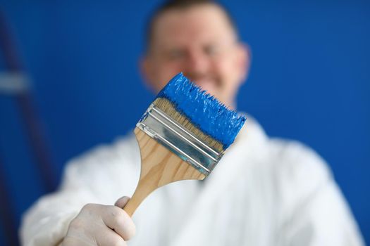 Painter worker hold brush covered in blue colour paint, handyman on construction site
