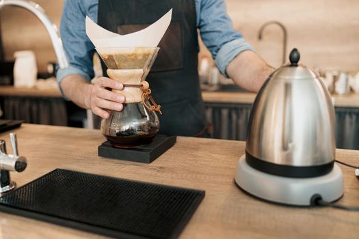 Male barista holding glass mug standing behind the counter