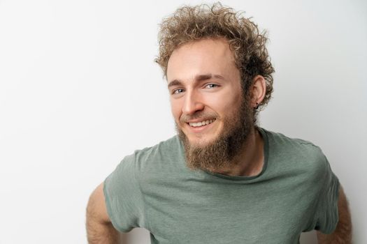 Handsome smiling young handsome bearded wild curly hair man with bright blue eyes isolated on white background. Young thinking man in green tshirt on white background