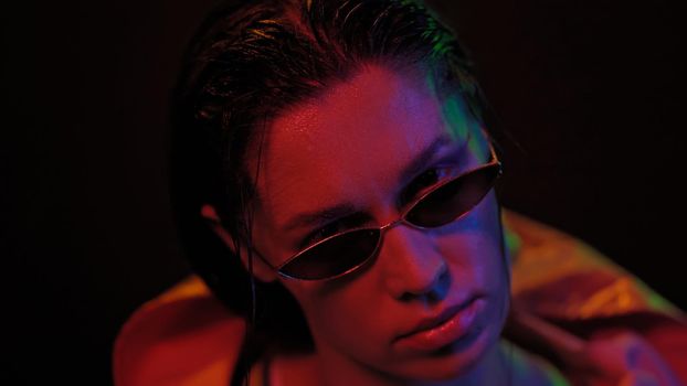 Portrait of young woman wearing jacket and sunglasses in neon color lights . Pretty girl in neon light on black background. Night club, Party concept