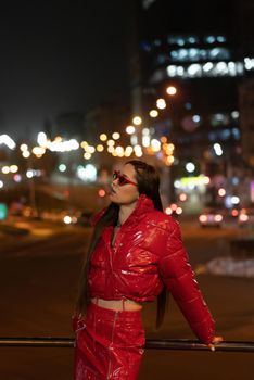 Fashion model girl with afri braid and red shiny skirt and winter coat standing outdoors in night city background. Night life concept. Night clubl life concept
