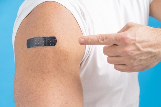 Close-up a man pointing finger on his shoulder with a band aid on it after receiving the Covid-19 vaccine. Vaccine against COVID-19 or coronavirus. Aging male skin. Fair skin men. Healthcare concept