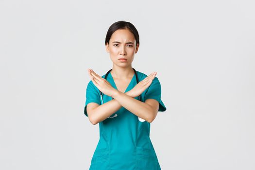 Covid-19, healthcare workers, pandemic concept. Displeased serious-looking concerned asian female doctor show cross gesture, want you stop, prohibit or forbid dangerous action, white background