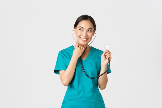 Covid-19, healthcare workers and preventing virus concept. Smiling cute asian doctor, female nurse examine patient lungs, using stethoscope, listening closer, standing white background