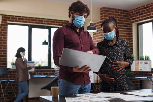 Multi ethnic diverse office workers wearing facemasks against coronavirus analyzing financial data