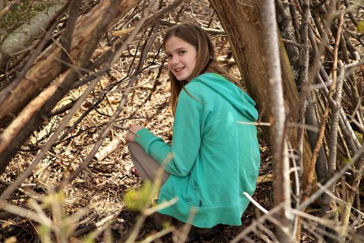 Young adolescent girl outside in the forest with lean-to tree fort treehouse tree house she built