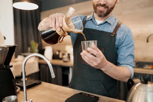 Smiling barista pouring filtered coffee into a glass