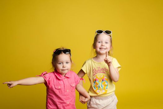Two happy beautiful stylish little girl wearing sunglasses posing isolated yellow studio background