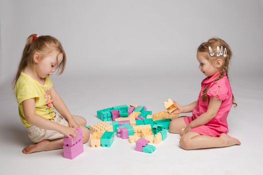 Two enthusiastic little girl playing assemble constructor full shot at studio white background