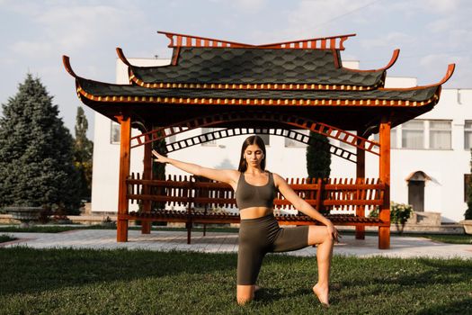 Qigong chinese meditation and sport training outdoor. Fit asian girl is meditating outdoor near chinese arbor.