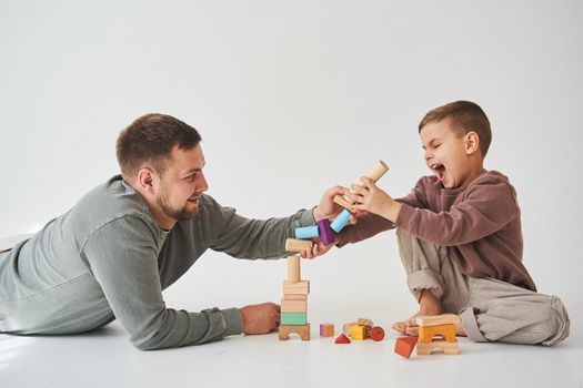Dad and son smiling, having fun and playing colored bricks toy on white background. Paternity. Caring father with his child.