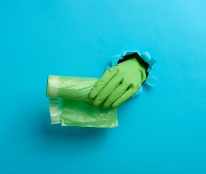  hand holds a bundle of transparent garbage bags on a blue background. A part of the body sticks out of a torn hole in the paper