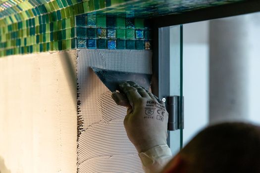 Worker applying mosaic tiles, bath or sauna renovation