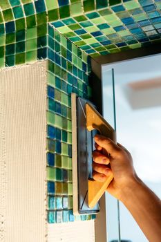 Worker applying mosaic tiles in bathroom walls