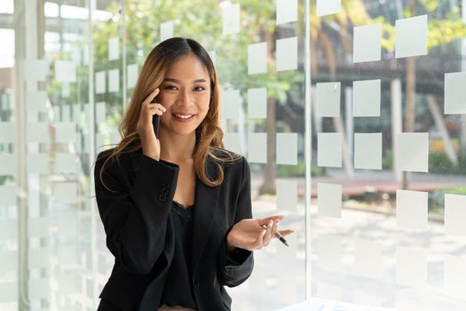 Portrait confident business asian woman calling on mobile phone at office window