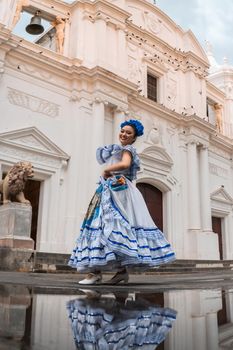 Vertical photo of a traditional dancer from Nicaragua in front of a puddle where you can see her reflection and the cathedral church of Leon de Nicaragua