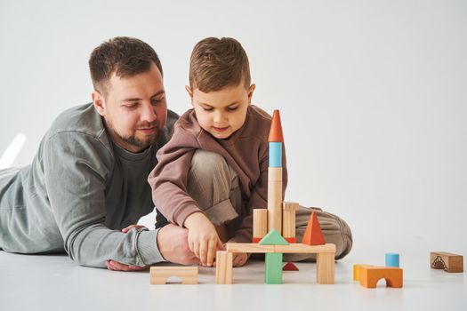 Paternity. Son and dad playing with colored bricks toy on white background. Father takes care of his kid.
