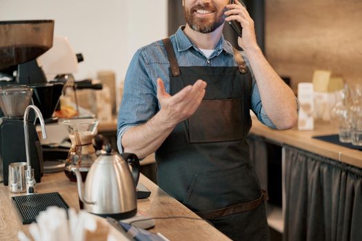 Smiling barista talks phone standing behind counter at coffee shop