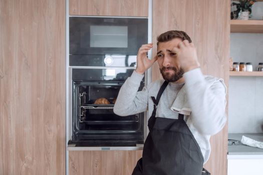 surprised man standing near the oven with burnt croissants.