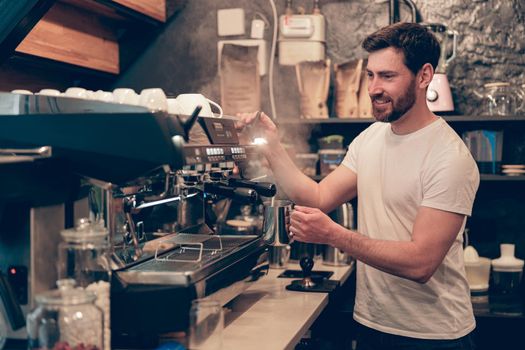 Caucasian happy male bartender making coffee at professional machine. Work in cafeteria.