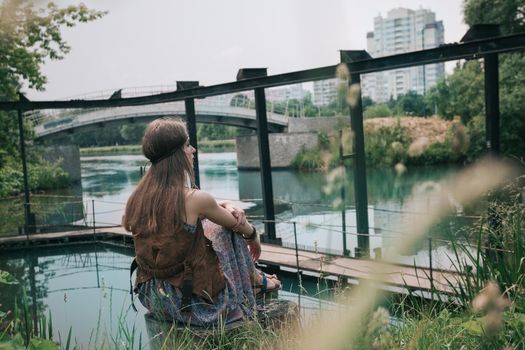 young hippie woman sitting near a city pond