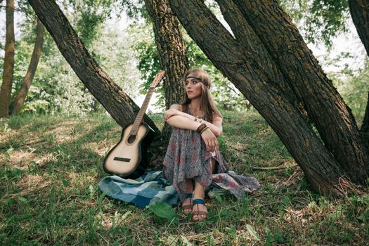 hippie woman with guitar sitting near a tree in the forest