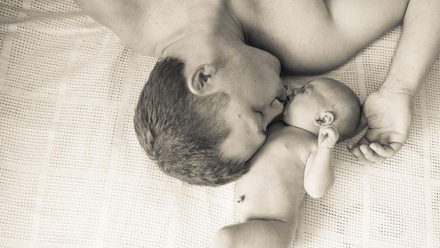 black and white photo. a happy father sleeps next to his newborn daughter.