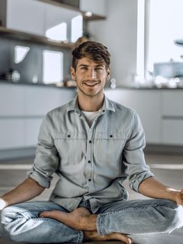 smiling young man sitting in Lotus position on kitchen floor