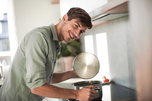 happy young man looking into a pot of delicious food.