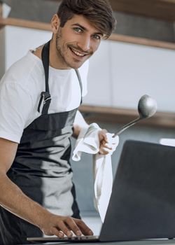 young man looking at laptop screen while cooking dinner