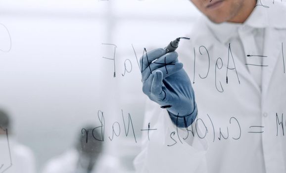 serious scientist writes a formula on a glass Board